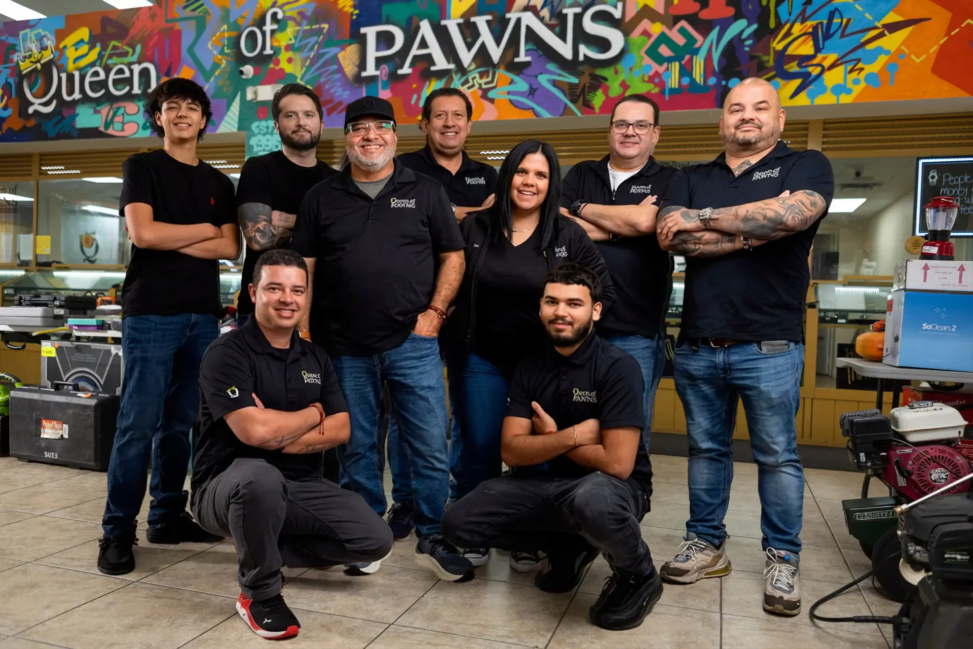Queen of Pawns team in front of the store mural